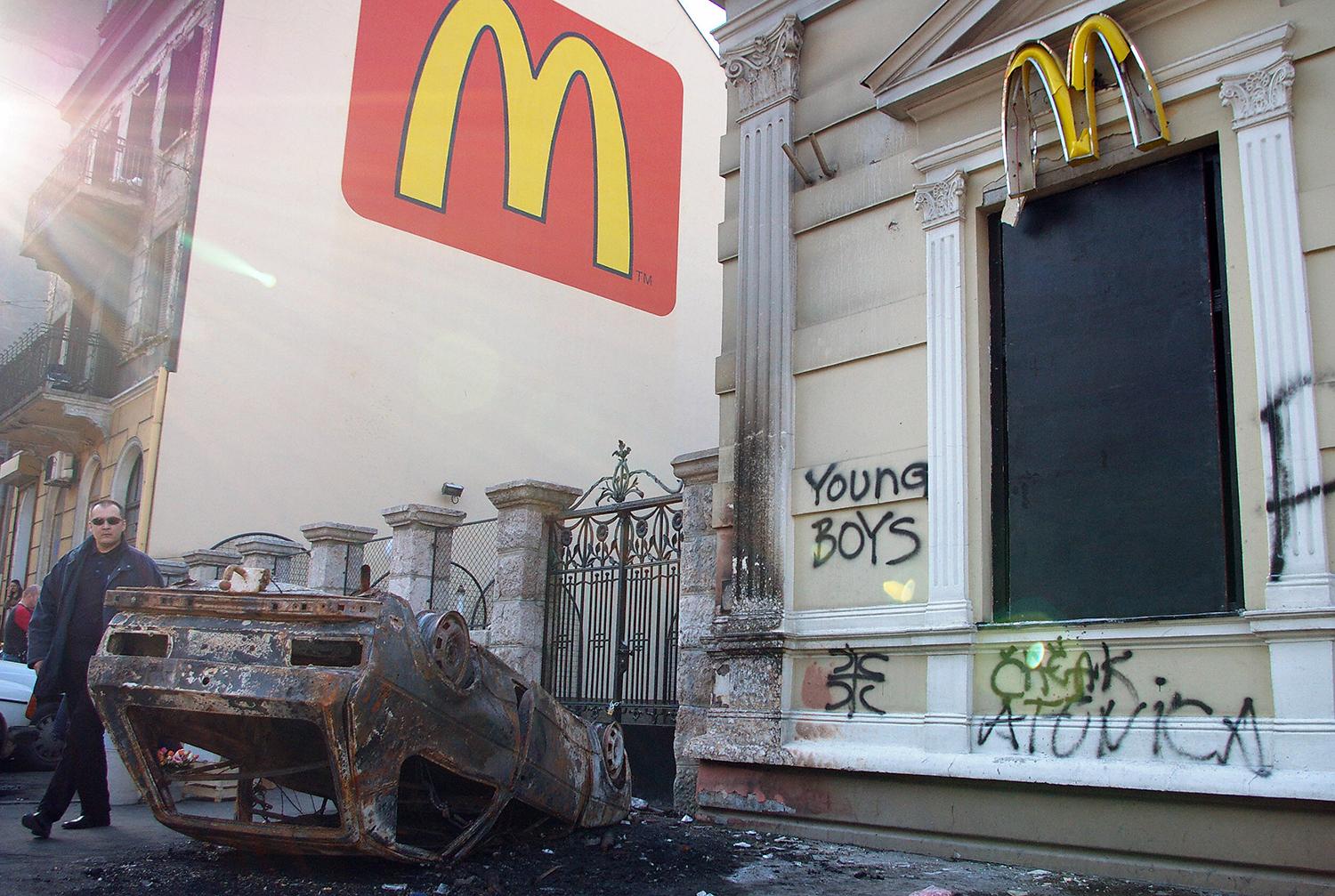 Pješak šeće pored zapaljenog automobila ispred restorana McDonald’s nakon nemira u centru Beograda 22. februara 2008.. - Avaz