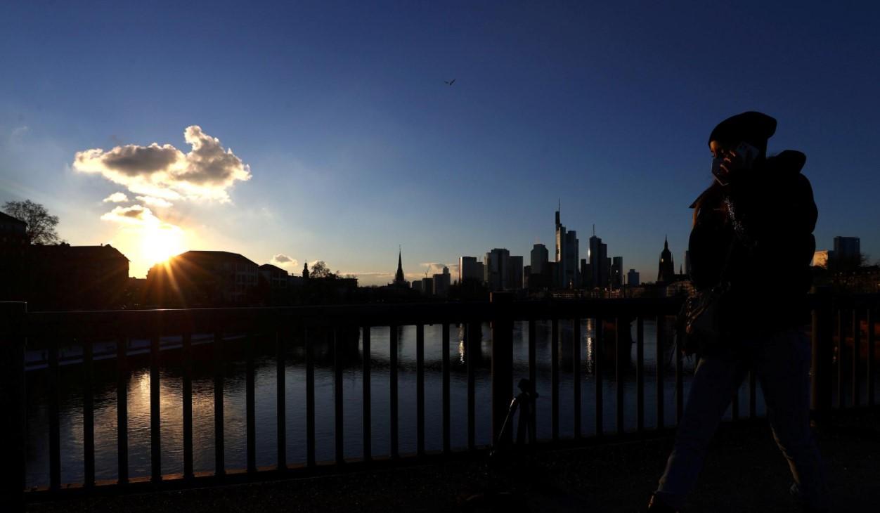 A woman wears a protective mask as she crosses a bridge in front of the skyline as the spread of the coronavirus disease (COVID-19) continues during an extended lockdown and a demand by the German government for more home office possibilities in Frankfurt, Germany, February 11, 2021. - Avaz