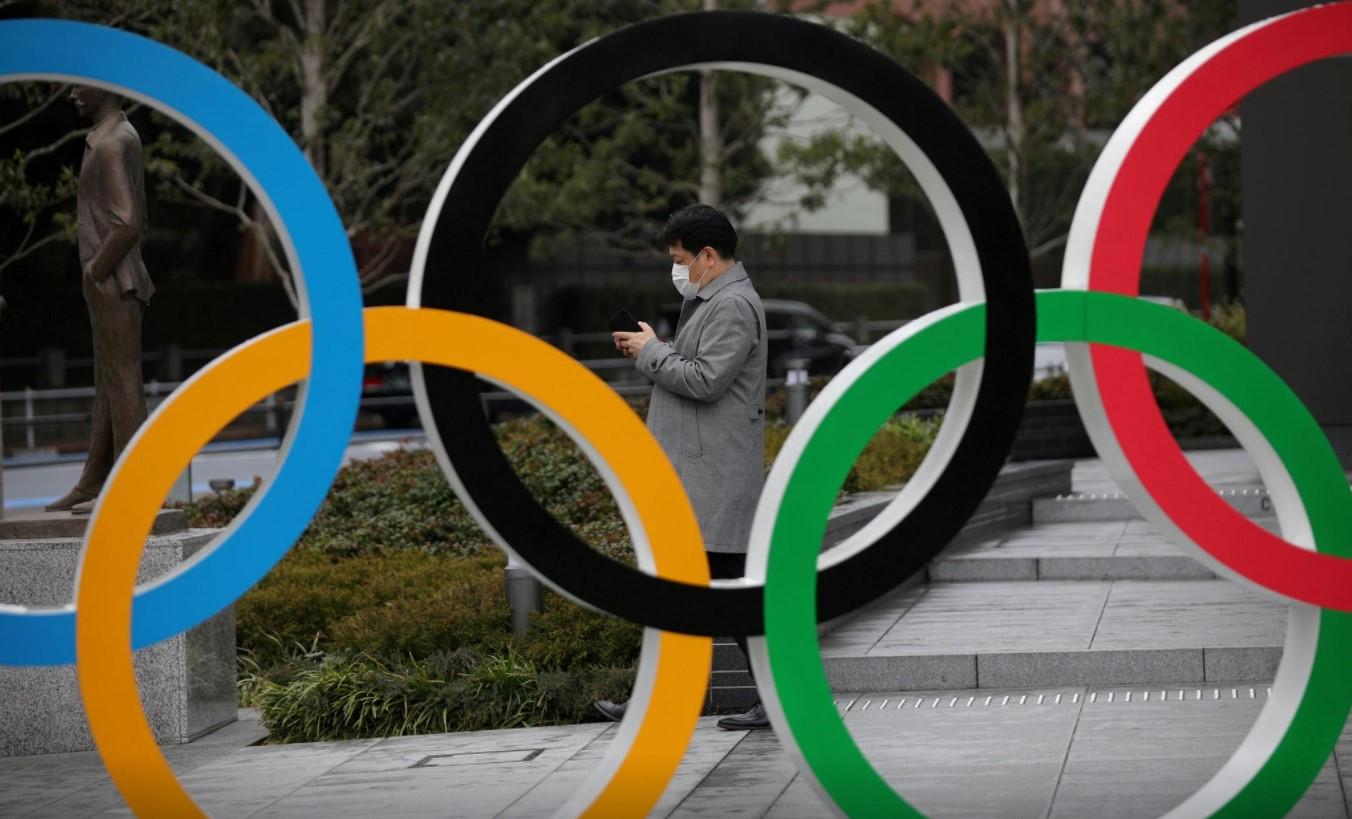 A man looks at his mobile phone next to The Olympic rings in front of the Japan Olympics Museum in Tokyo, Japan, March 4, 2020. - Avaz